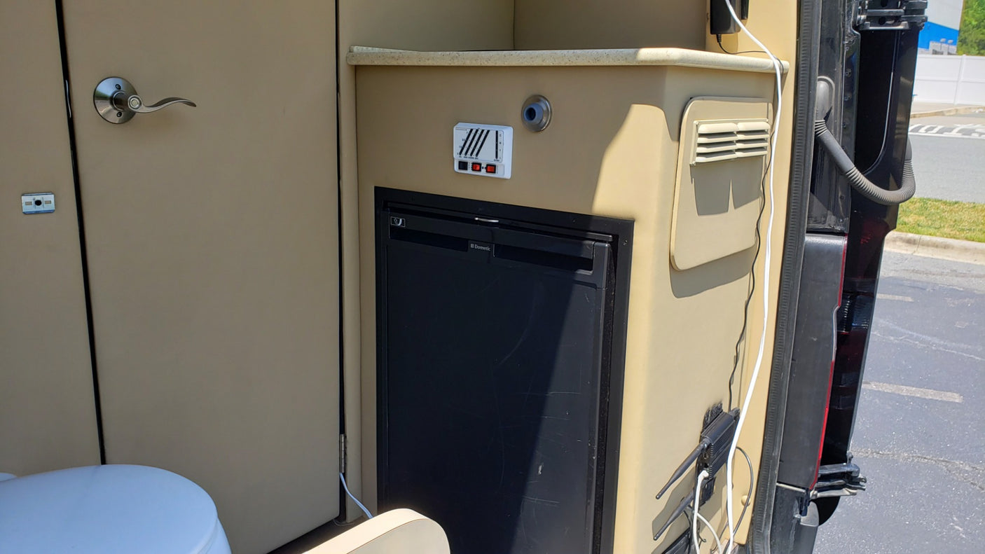 RV rental interior features Dometic fridge, toilet, and control panel in a compact campervan setup.