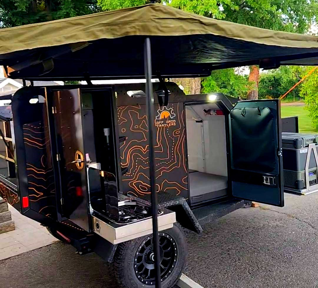 Get ready for adventure! This black off-road trailer RV rental has an open kitchen, sleeping area, and shade awning.