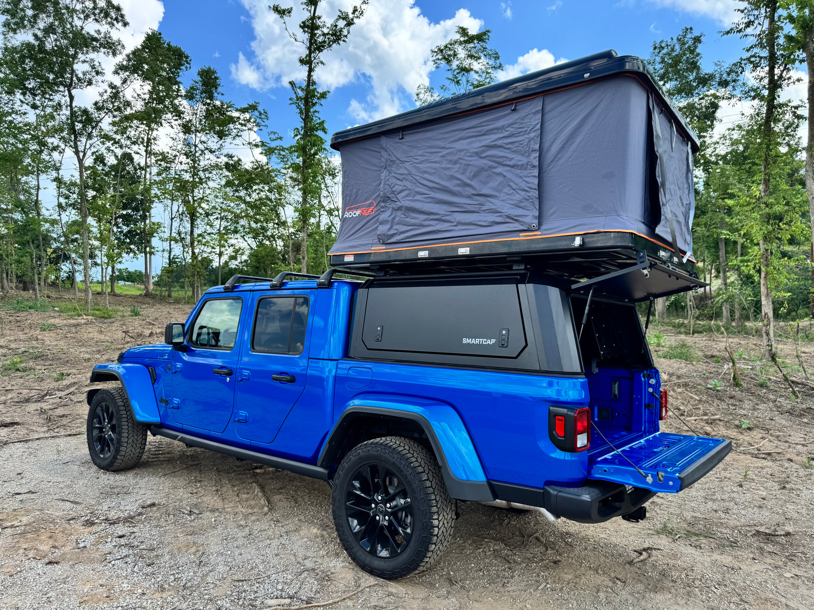 Blue Jeep Gladiator with open rooftop tent & bed cap. Ready for adventure, ideal for an RV rental or overlanding trip.