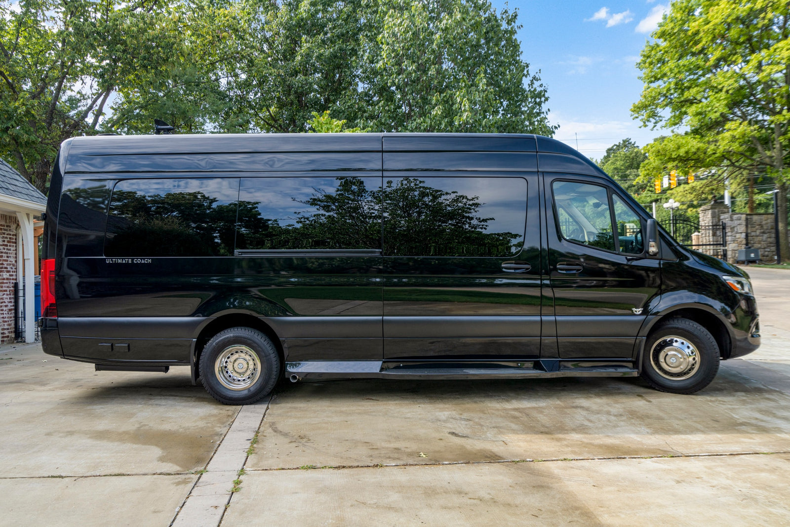 Side view of a sleek black Ultimate Coach RV rental van, parked on a concrete driveway.