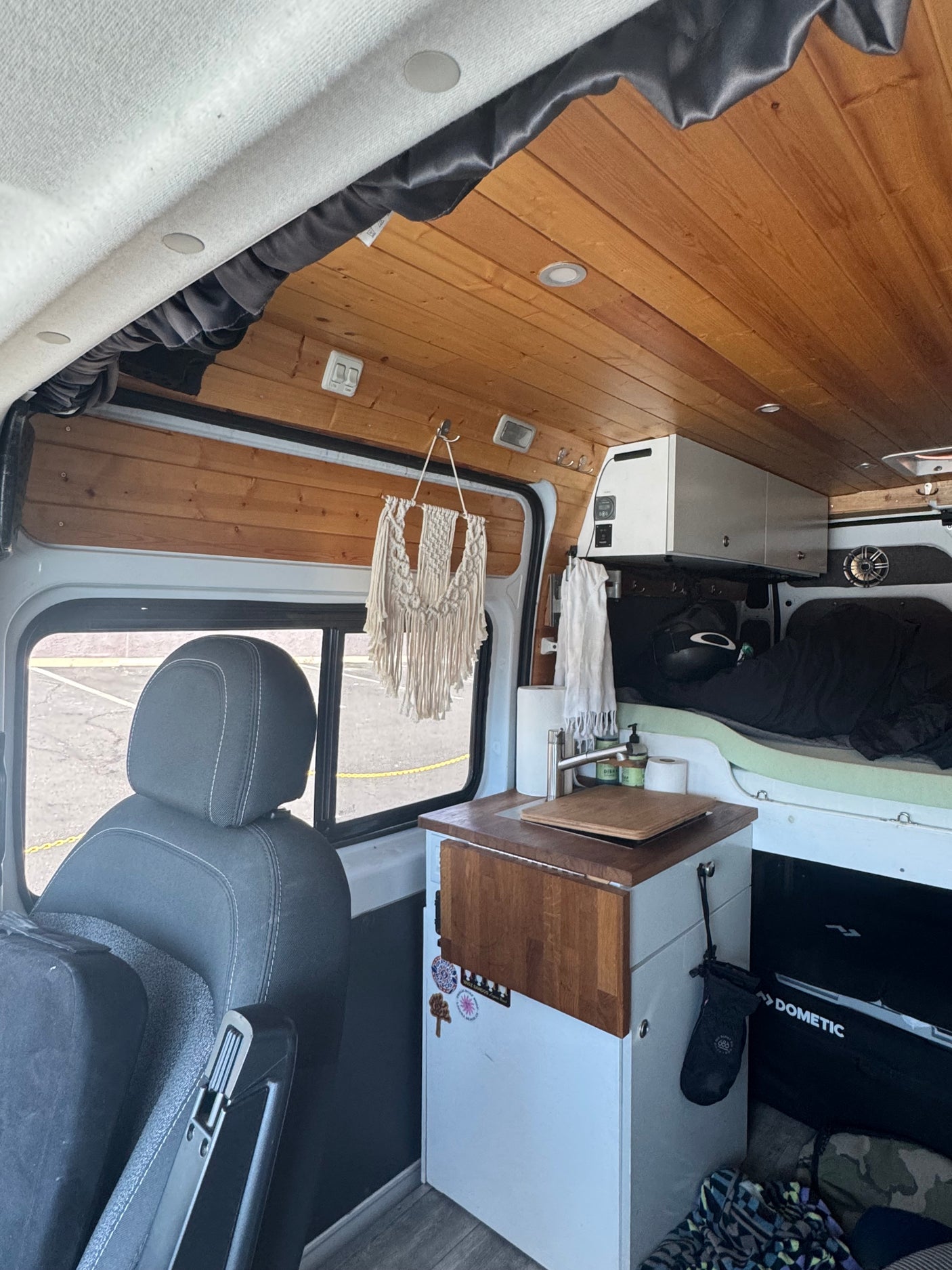 This cozy RV rental interior features a beautiful wood-paneled ceiling, compact kitchen with a sink, and a comfortable bed area.
