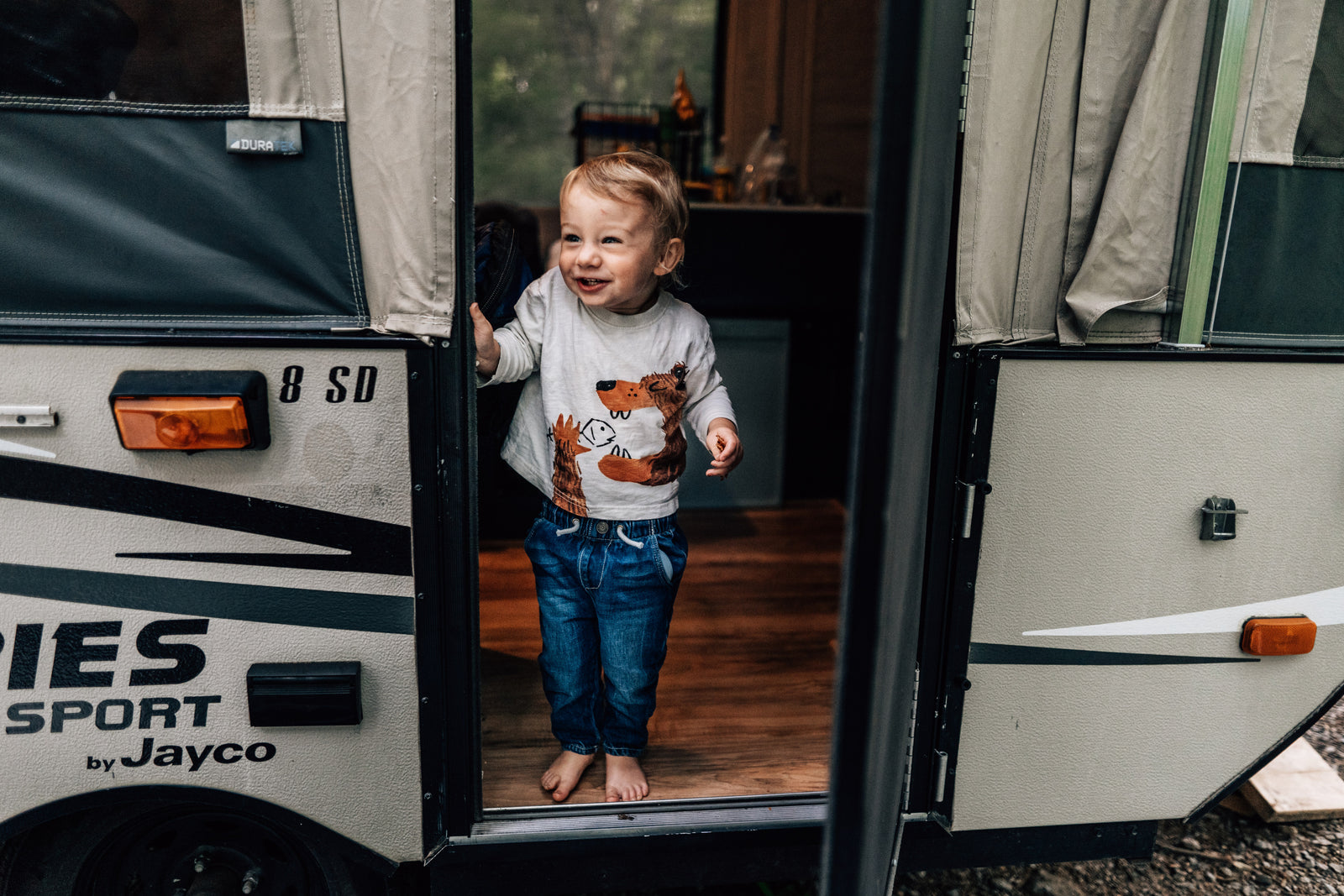 Happy toddler smiles from a Jayco Sport pop-up camper, a perfect rv rental for family adventures.
