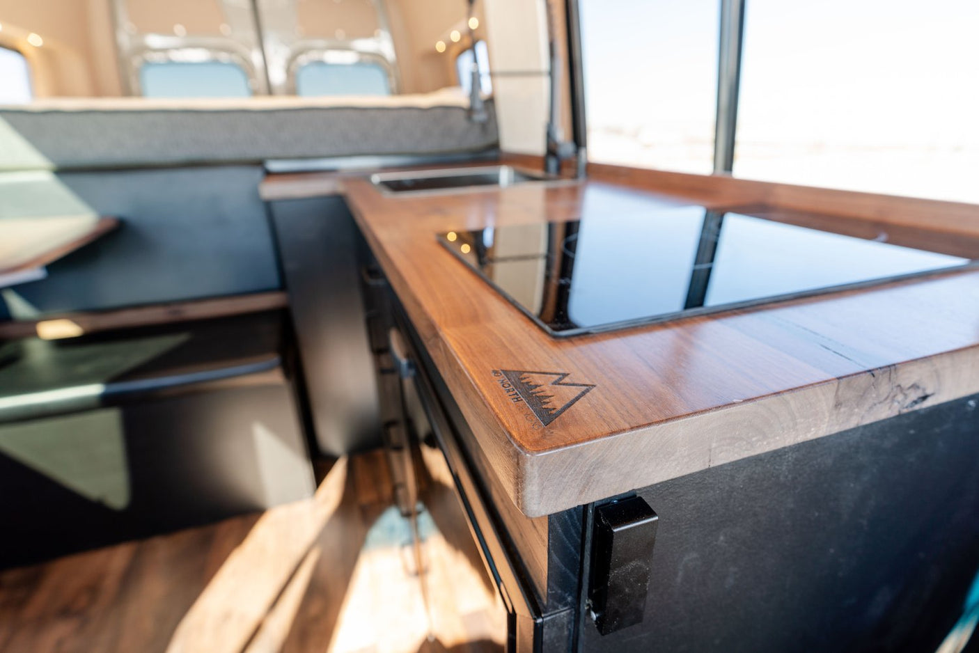 RV rental van's 46 NORTH LONG kitchen: sleek wooden countertop, induction cooktop & sink. Compact living on the go.