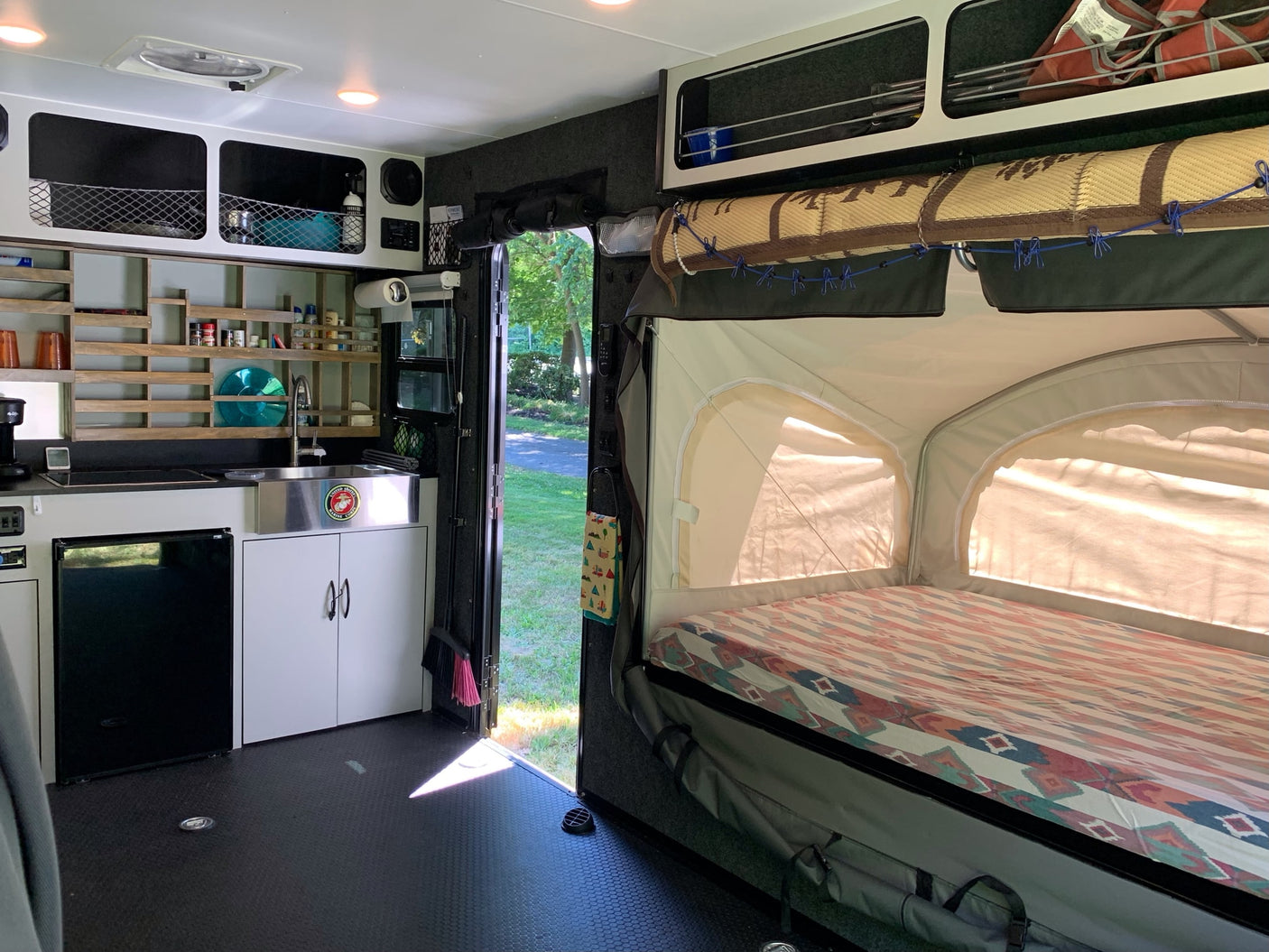 Inside a cozy rv rental: full kitchenette, smart storage, and a pop-out bed with patterned bedding. Ready for adventure!
