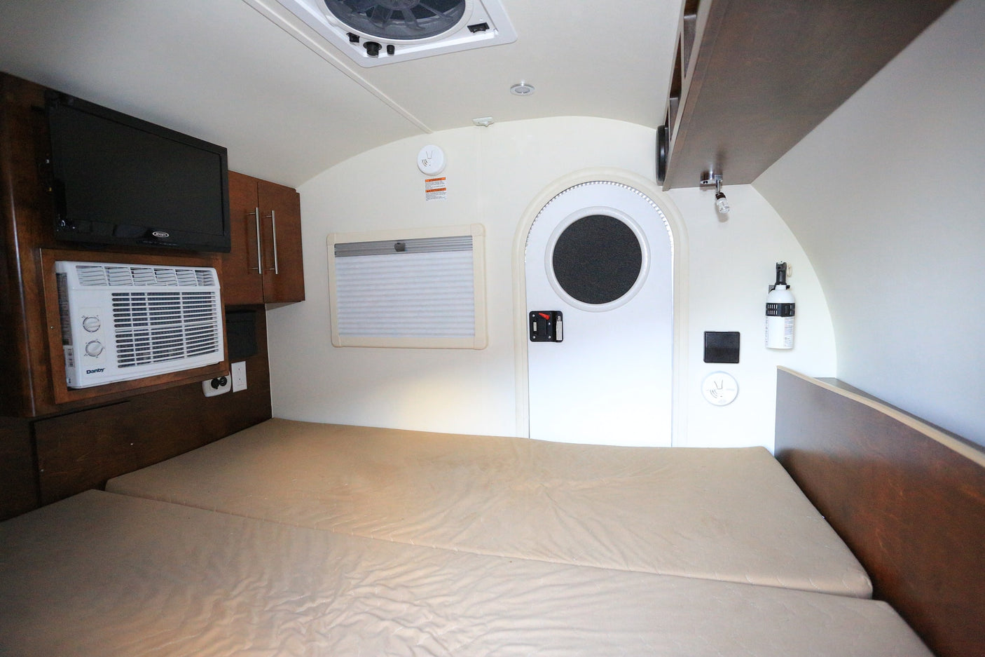 RV rental interior with a cozy bed, TV, AC, window, and a distinctive round door.