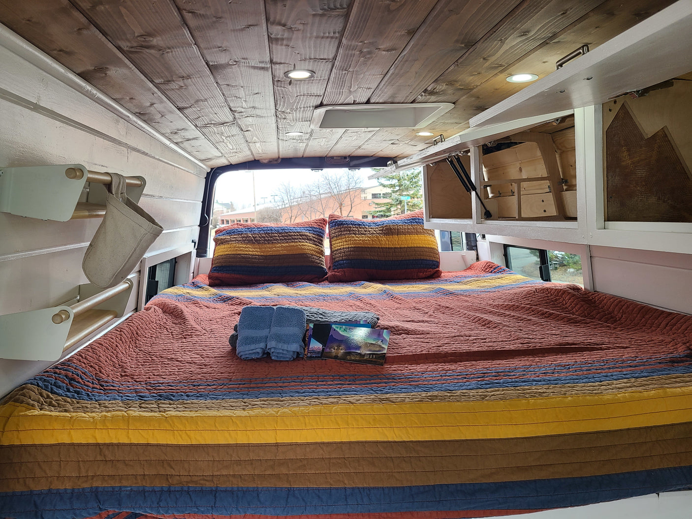 Cozy RV rental interior with a comfortable bed, wooden ceiling, and smart storage. Perfect for your next adventure.