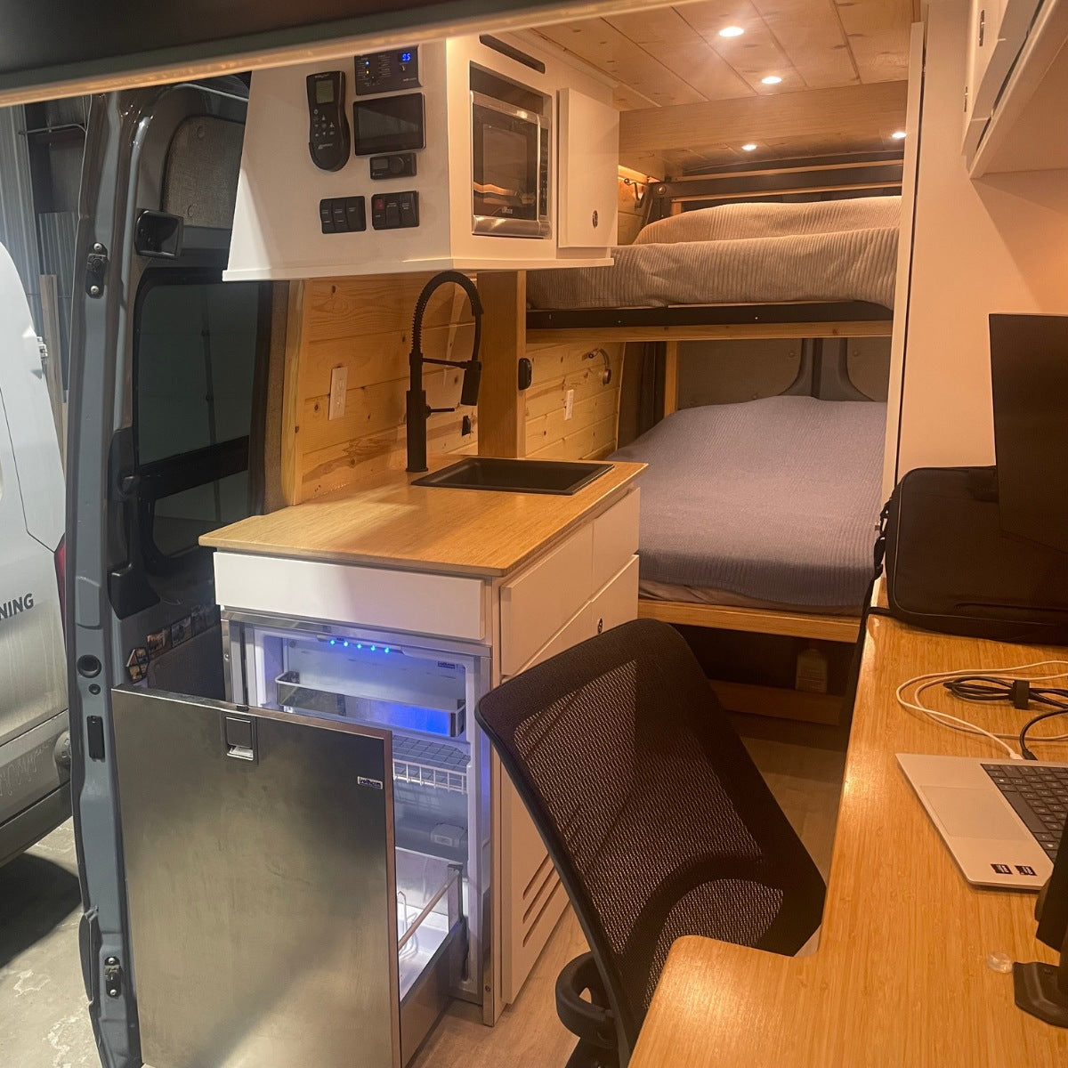 View inside an rv rental: functional kitchen, bunk beds, & workspace. Ideal for compact camper van adventures.