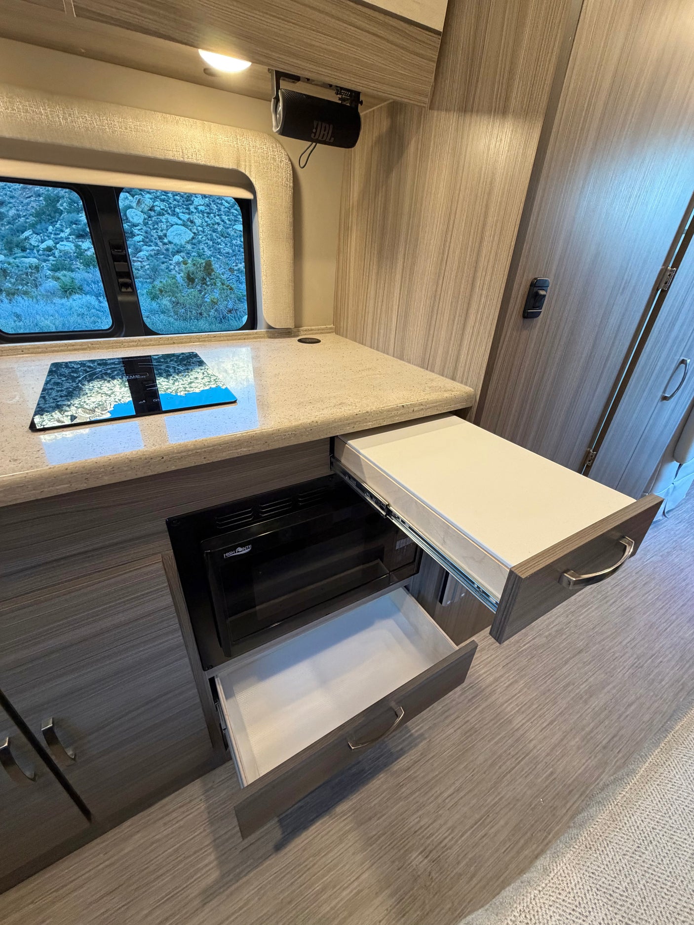 Modern rv rental galley featuring an induction cooktop, microwave, and open drawers. A JBL speaker is mounted overhead.