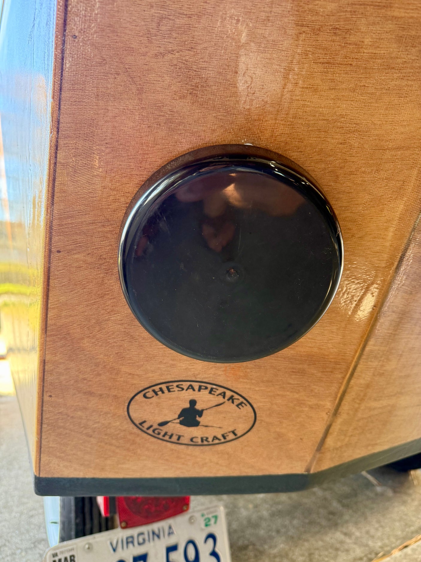 Wooden kayak/boat with round black hatch & Chesapeake Light Craft logo. Visible near a vehicle, possibly an RV rental trailer.
