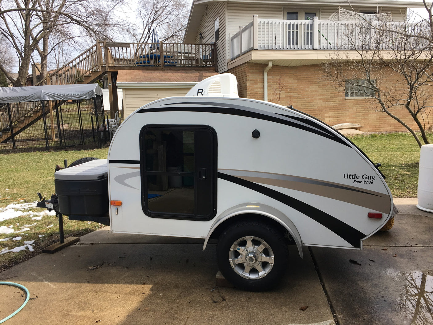 A white teardrop RV, labeled 'Little Guy', parked on a driveway. Consider this unique rv rental.