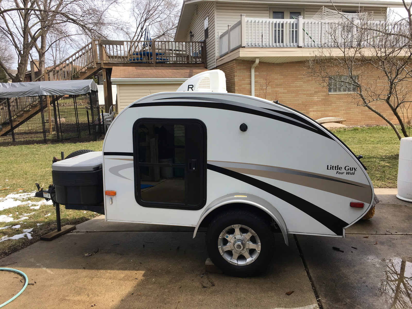 A white teardrop RV, labeled 'Little Guy', parked on a driveway. Consider this unique rv rental.