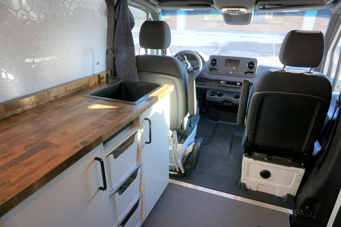 RV rental: Inside a modern camper van, featuring a tiled kitchen, wood counter, sink, and front cabin view.