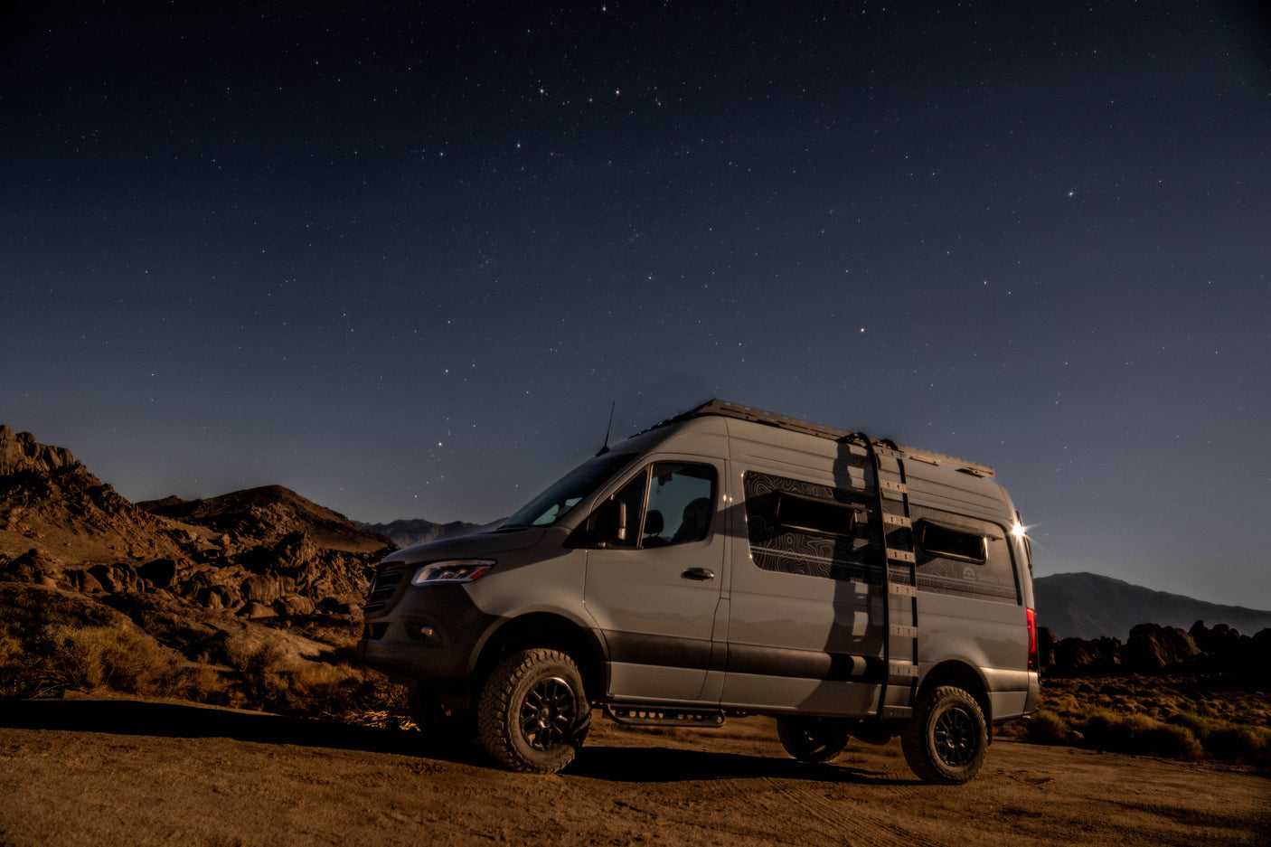 Starry nights and adventure await! This off-road camper van, perfect for RV rental, is parked under a clear night sky in a rocky desert.