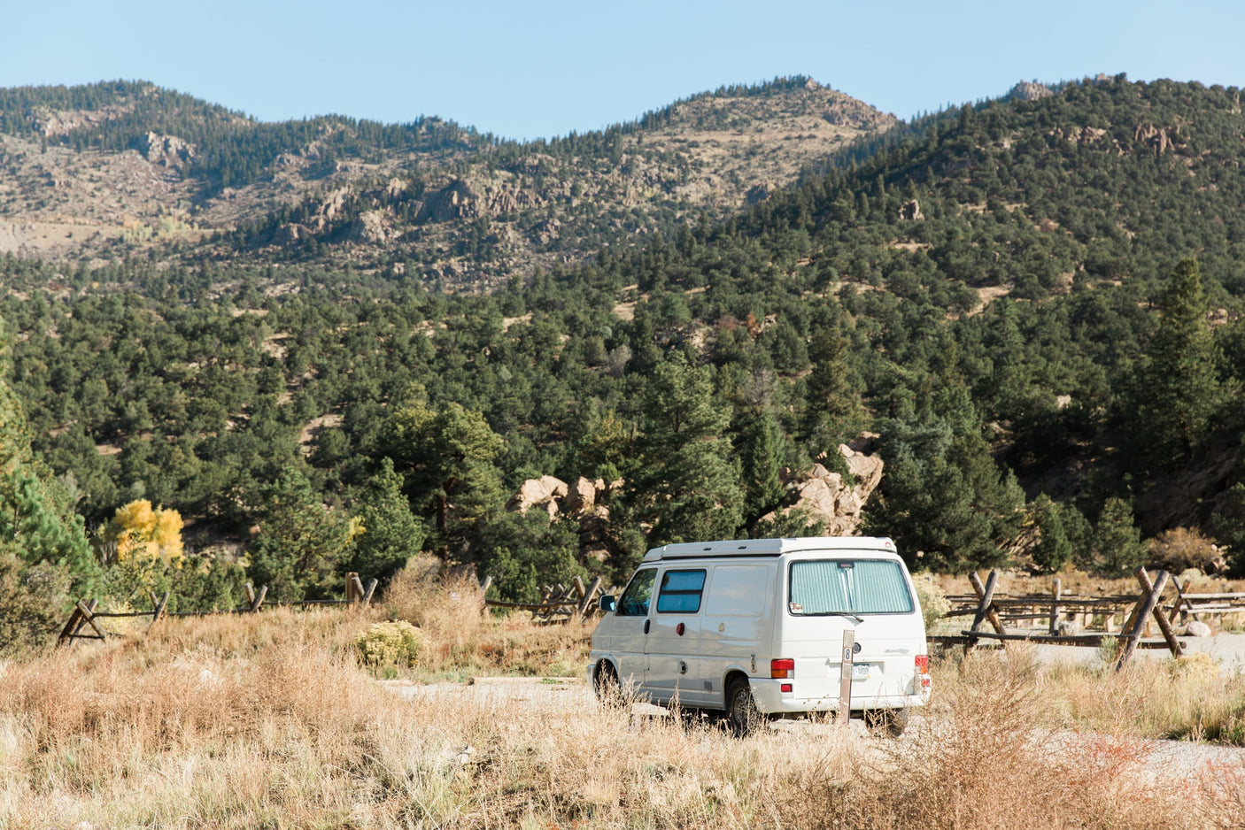 White camper van, an RV rental, parked in scenic autumn mountains with dry grass & pine forests. Ideal travel.
