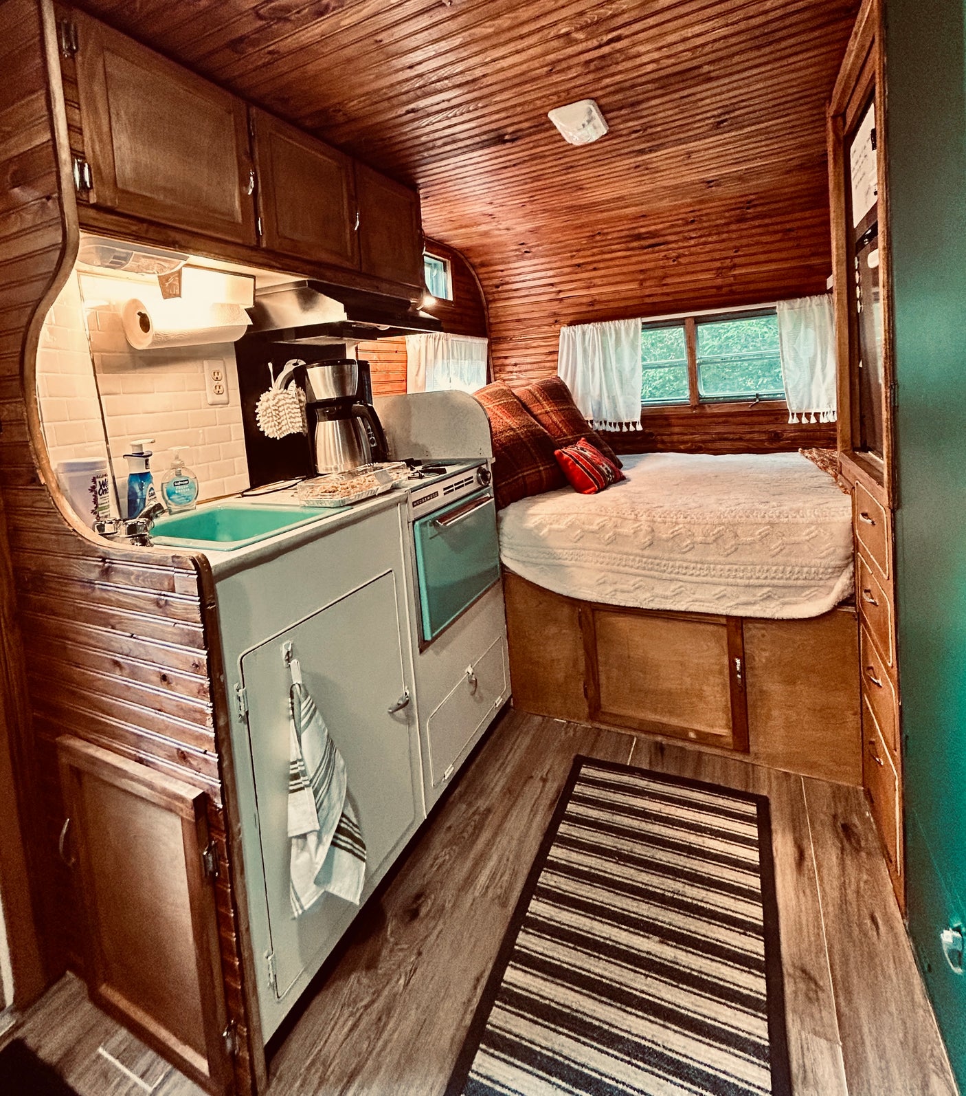 RV rental: Rustic RV interior with wood paneling, a compact kitchen featuring a light blue stove, and a comfortable bed area.