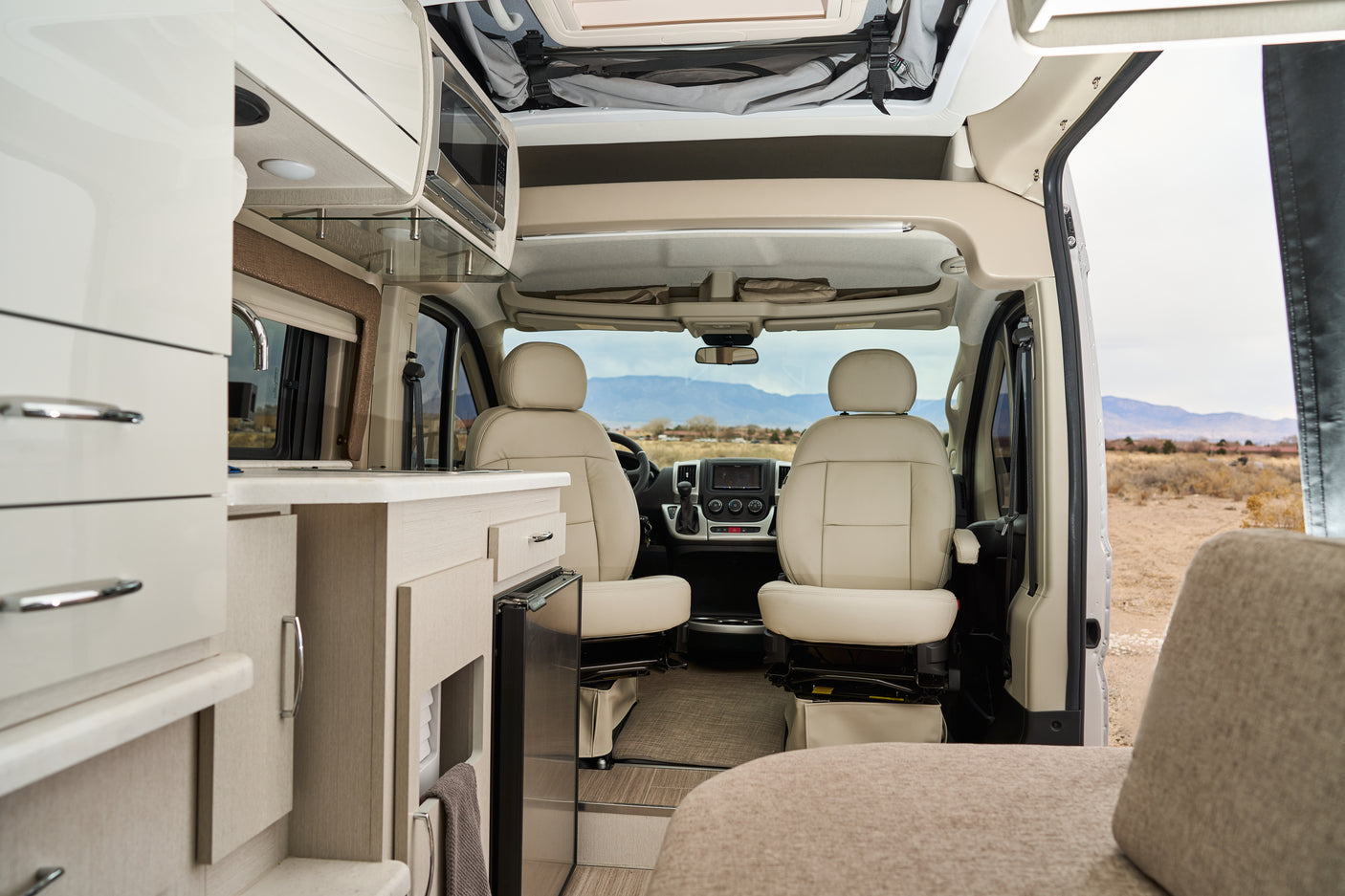 Bright rv rental interior featuring a modern kitchenette, comfortable swivel front seats, and scenic mountain views.