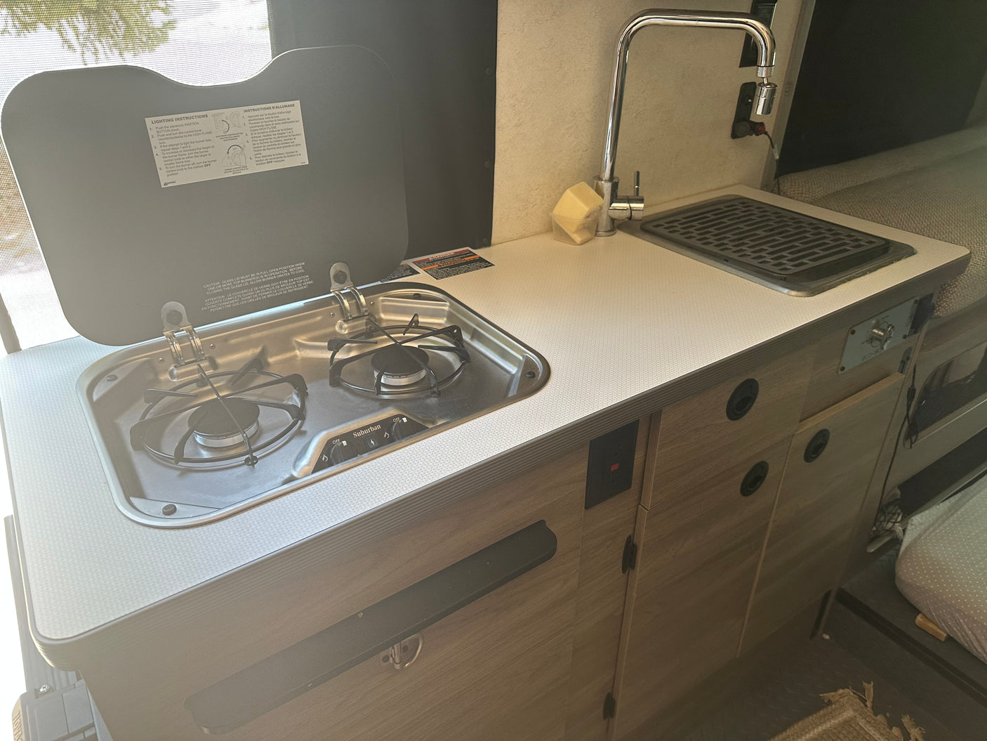 Compact RV rental kitchen featuring a two-burner stove, sink with faucet, and counter. Perfect for camping meals.