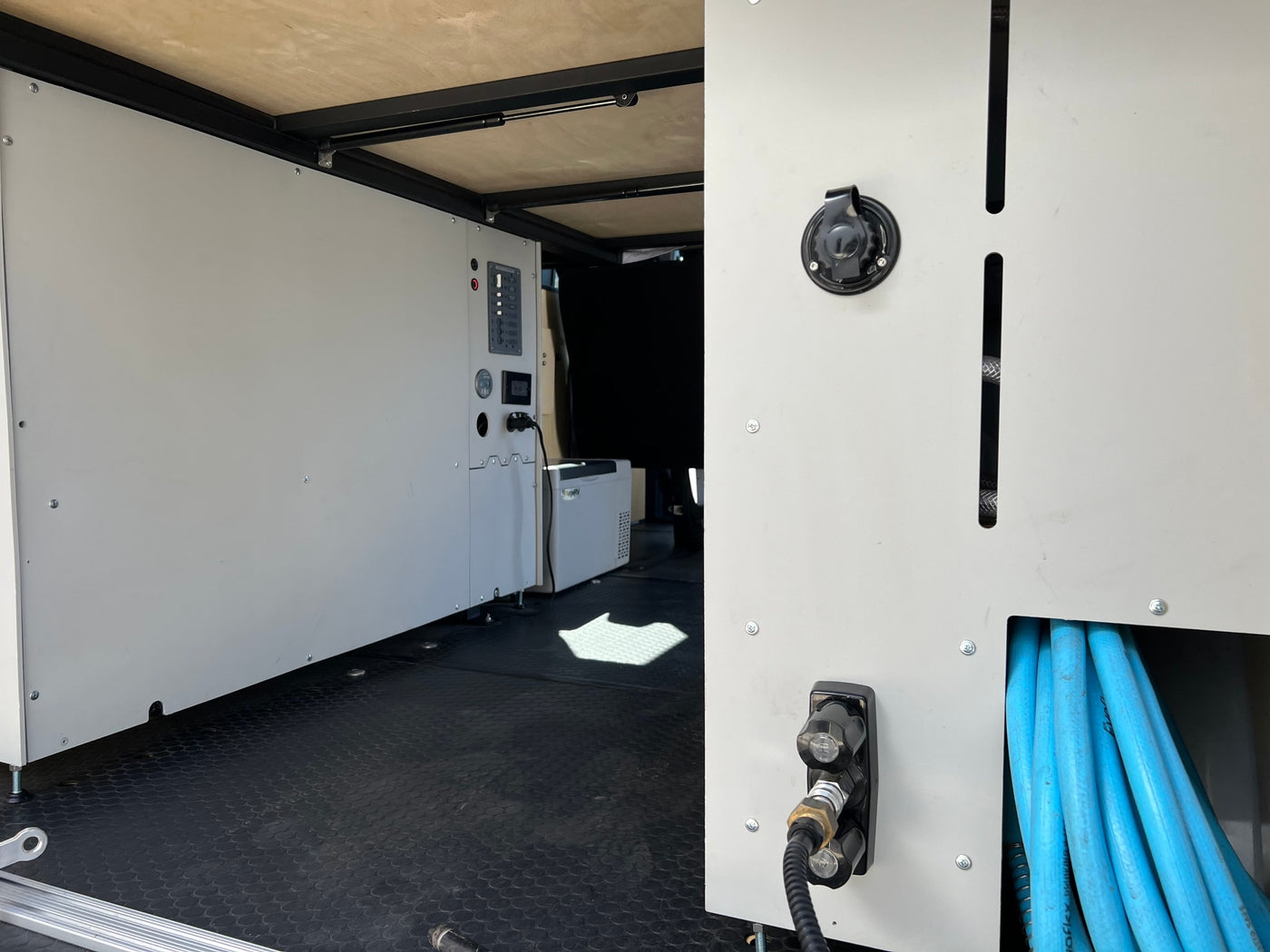 RV rental interior: organized utility panel with power, water connections, and hose storage in a customized camper van. — photo 5