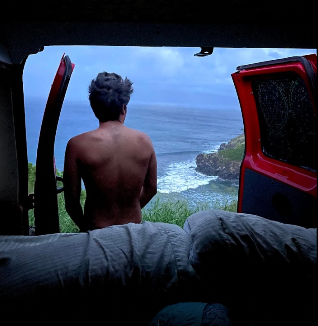 A man, seen from behind, enjoys a stunning ocean view with crashing waves from his RV rental, parked on a rugged coastline.