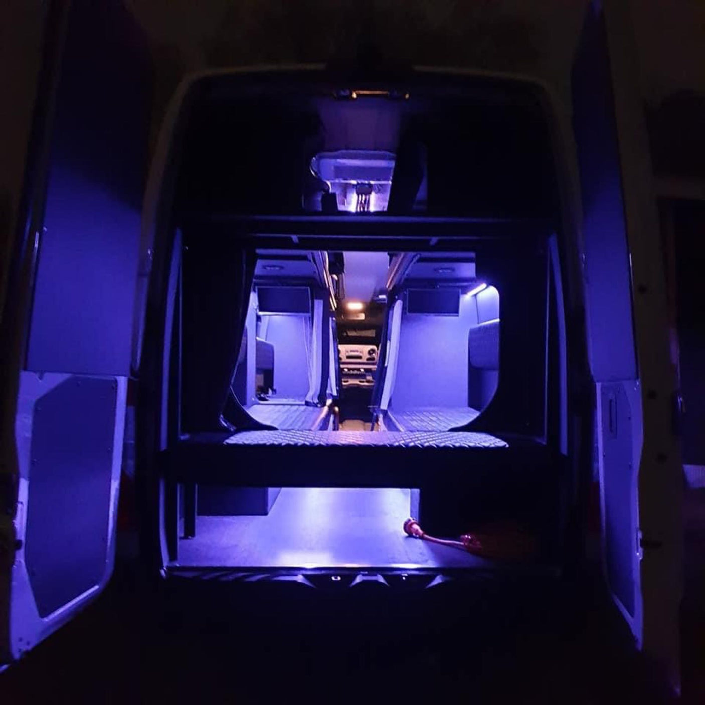 and bright red LED lighting creating a lounge vibe.|Spacious RV rental interior with comfortable diamond-quilted bunk beds and seating for road trips. Perfect for travel.|RV rental van conversion: Dark gray interior with large window