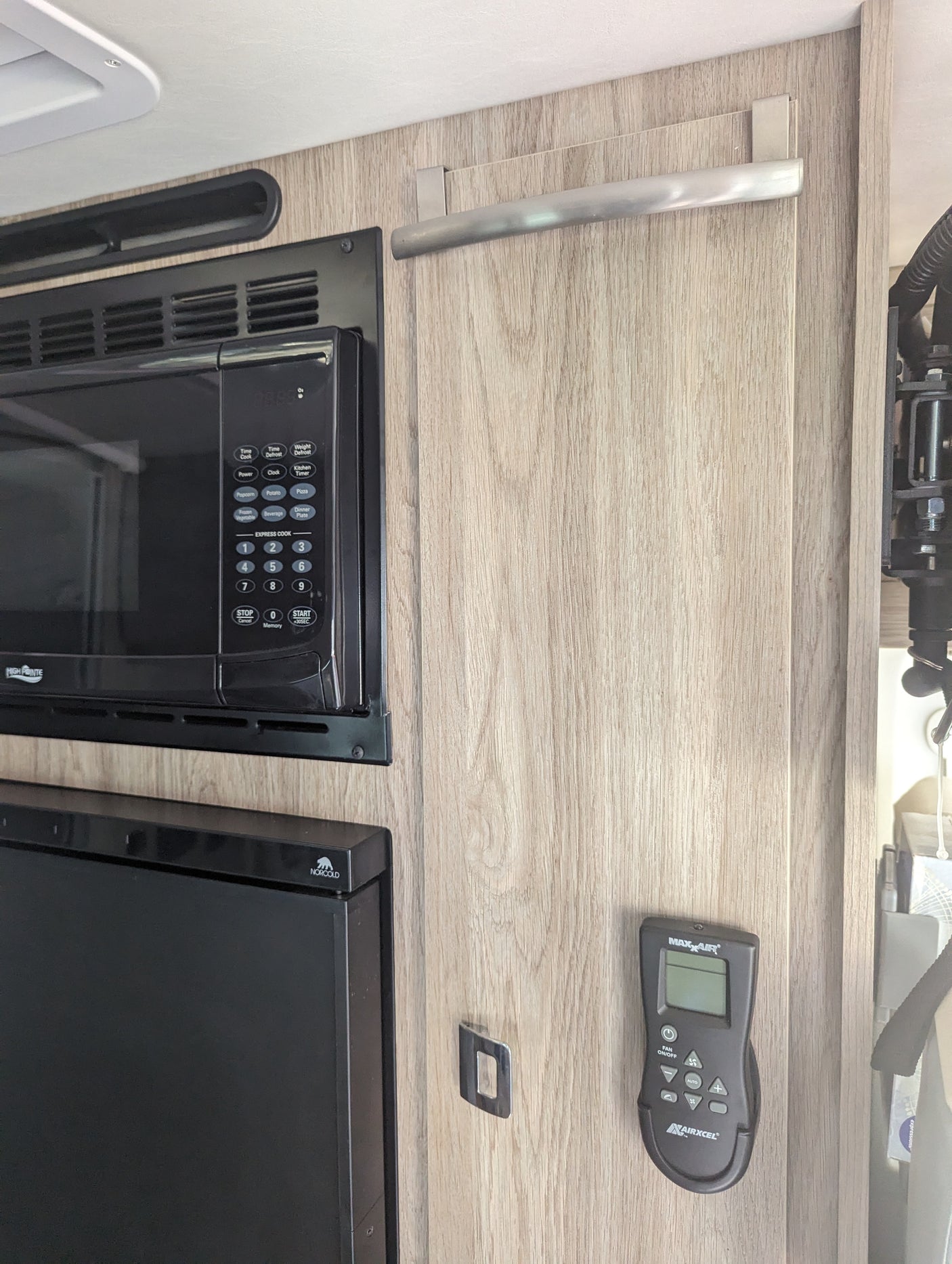 RV rental interior features a built-in microwave, Norcold refrigerator, and Maxxair fan control panel, all within a modern wood-paneled space.