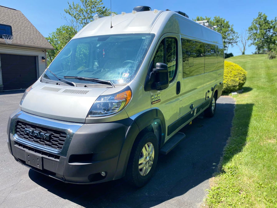 Front 3/4 view of a silver Ram ProMaster camper van on a sunny driveway