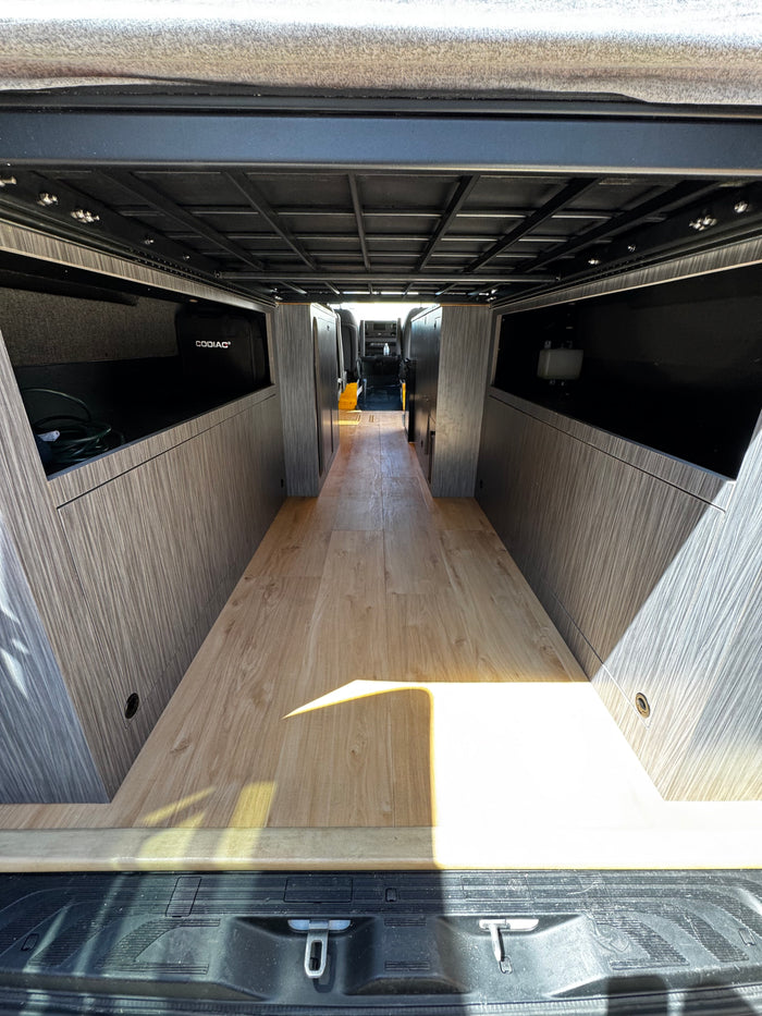 Spacious RV rental interior with wood floor, custom storage, and overhead frame for comfortable mobile living.