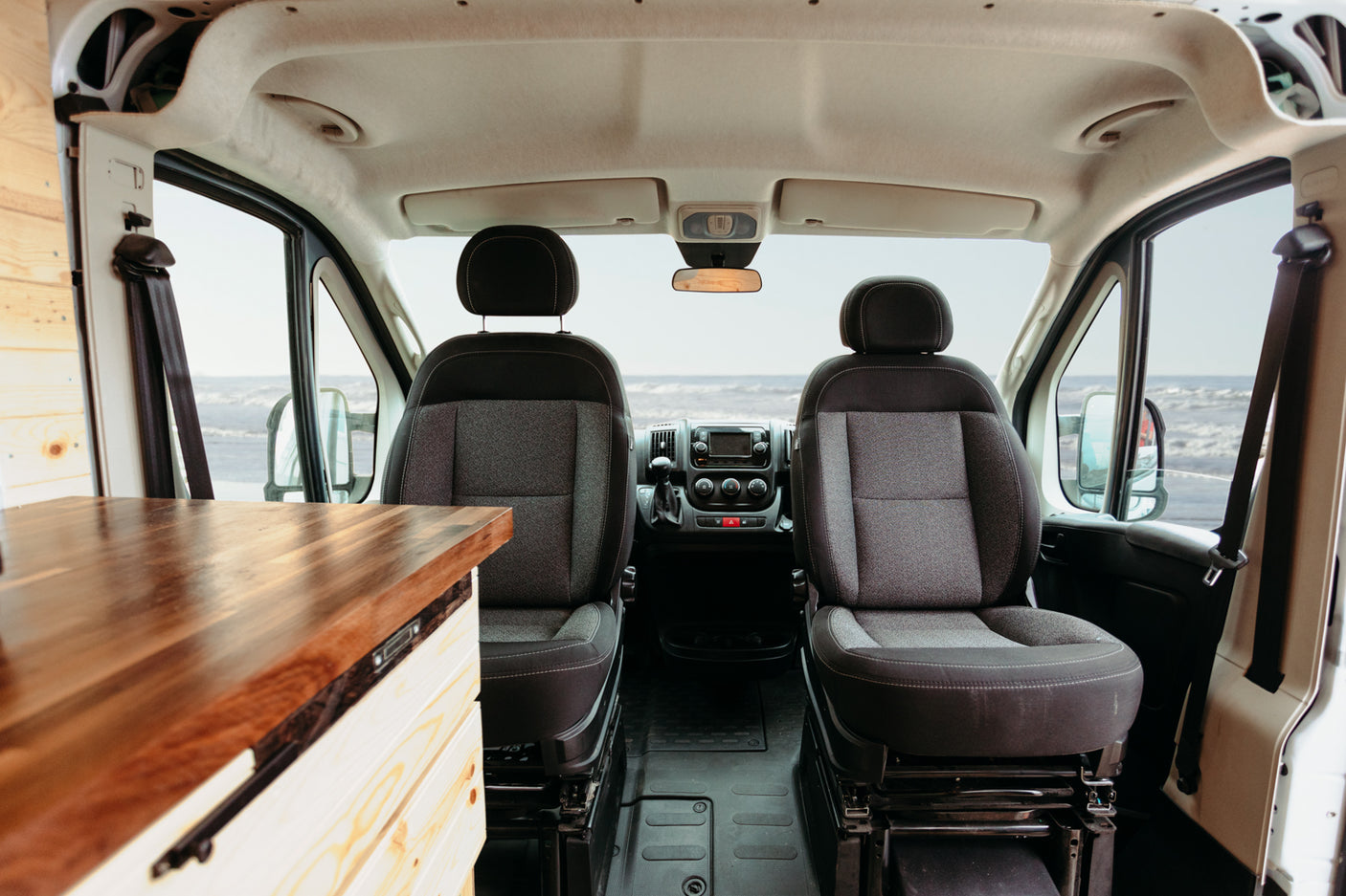 Experience road trip freedom! RV rental: Interior of a custom camper van with front seats & ocean view.