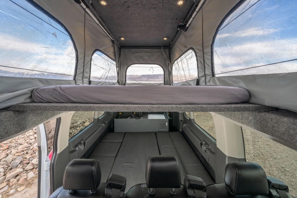 perfect for mobile living on your road trip.|View inside an rv rental: an elevated bed and a lower bed with light blue and beige bedding