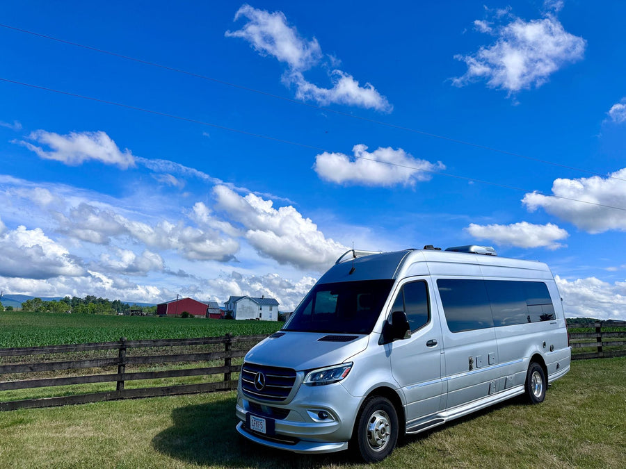 Silver Mercedes Sprinter RV rental in a rural field with a wooden fence