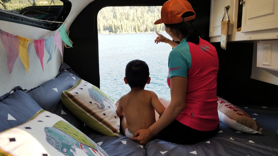 RV rental: A cozy family moment inside, watching the beautiful lake view. Mom points out details to child from bed.