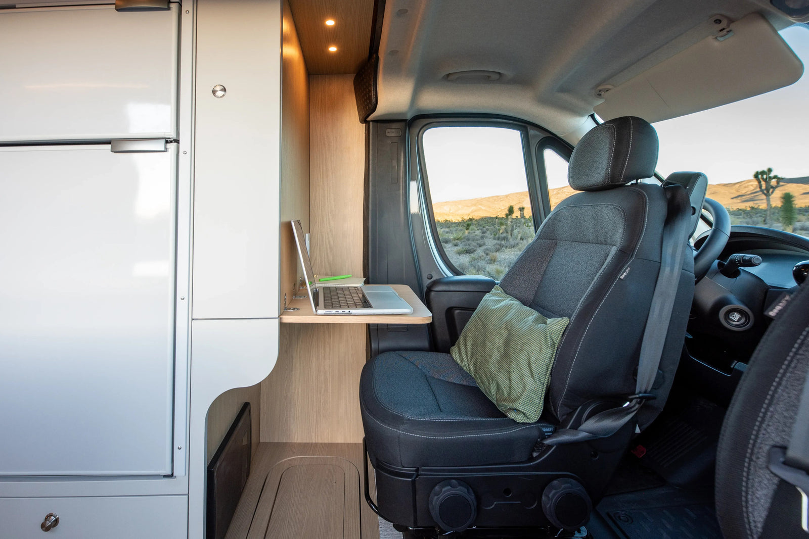 Modern RV rental interior: workspace with laptop, comfy seat, and stunning desert views through the window.