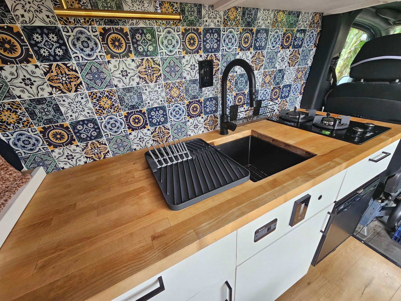 Stylish RV rental kitchen with vibrant tile backsplash, wooden counters, black sink & cooktop, ideal for travel.