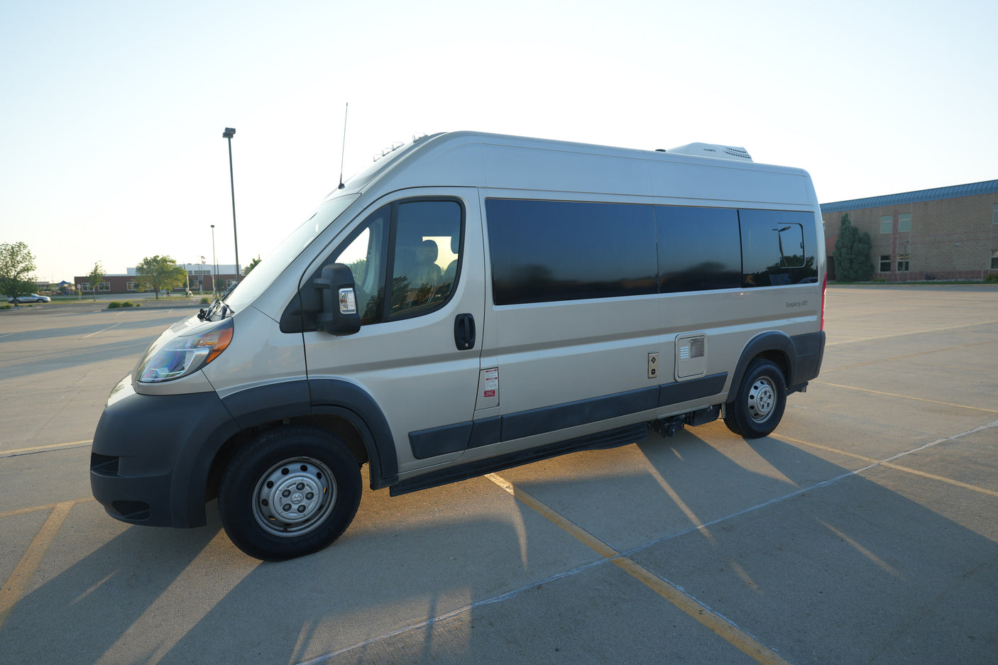 A light-colored camper van, an ideal RV rental, parked in a sunny lot, showcasing its sleek design and features.