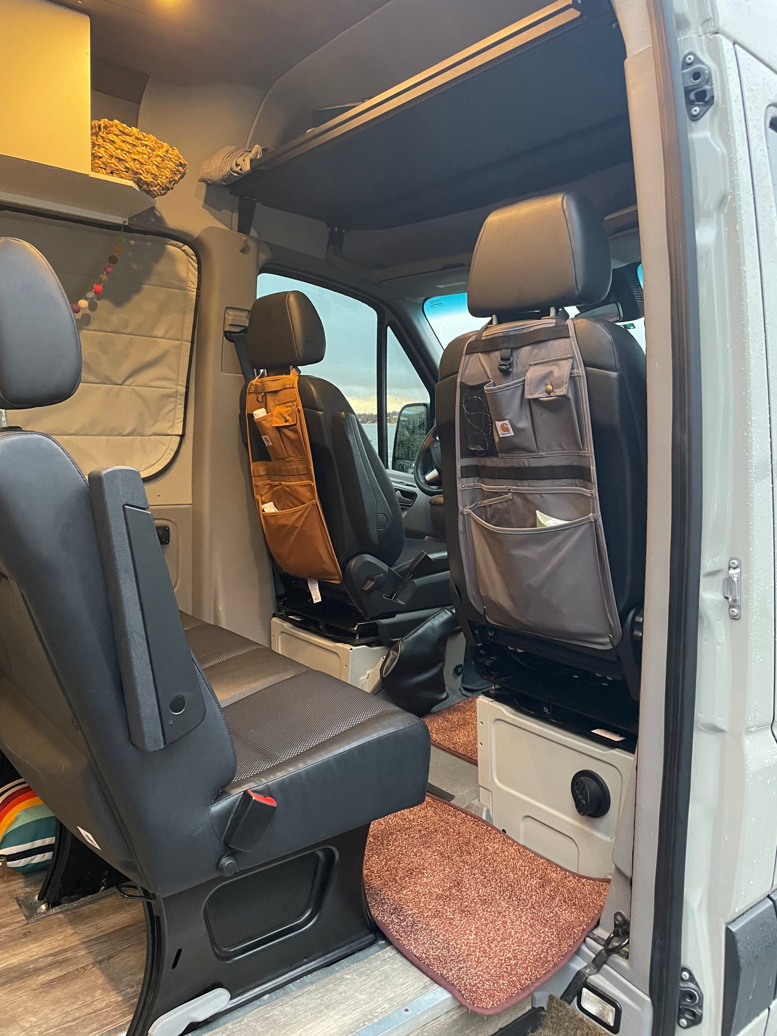 Inside an RV rental: swivel front seats with attached Carhartt organizers, custom overhead storage, & wood floor.