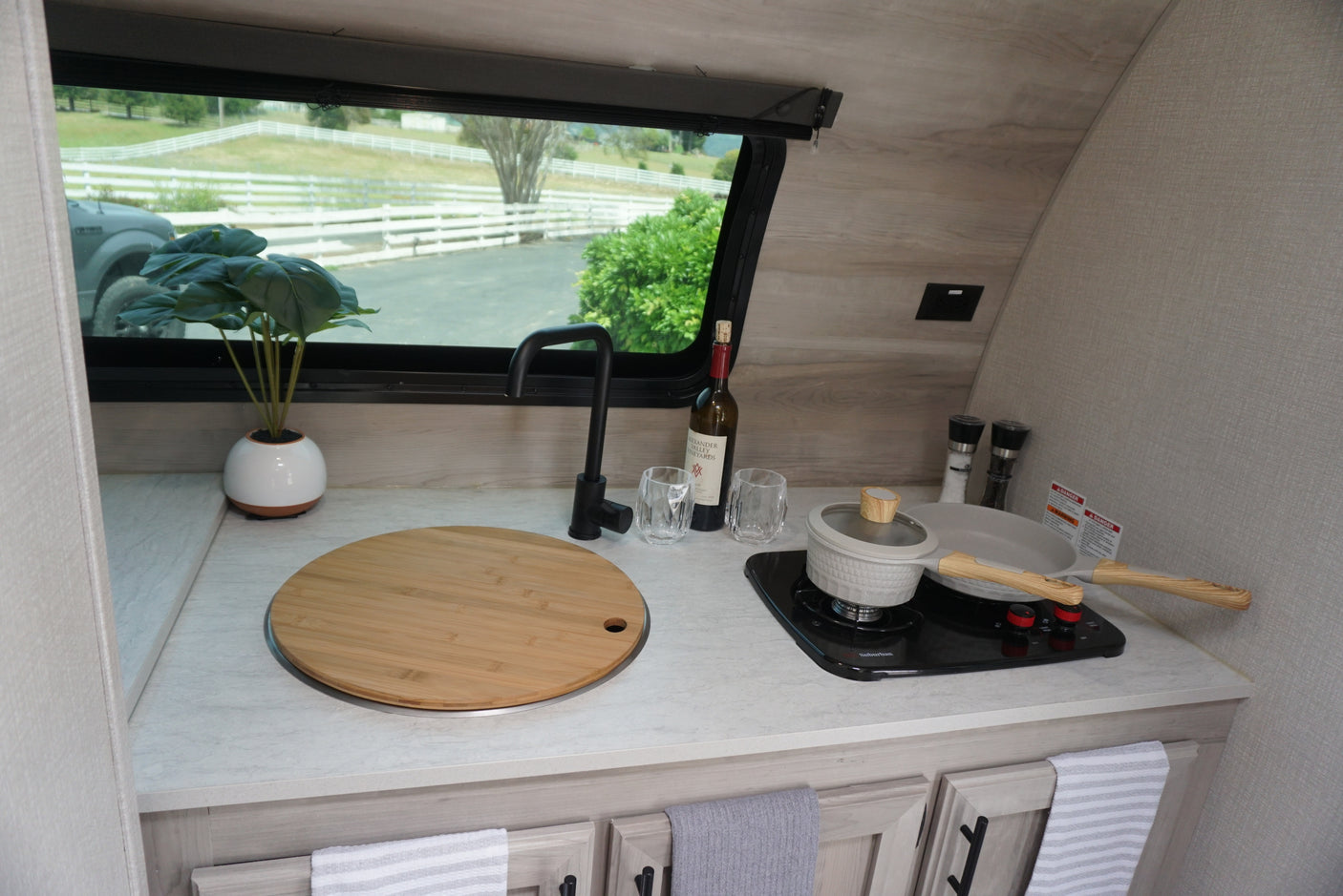 Get cooking in this cozy RV rental kitchen, featuring a sink, stovetop, and cookware. View of white fences outside.