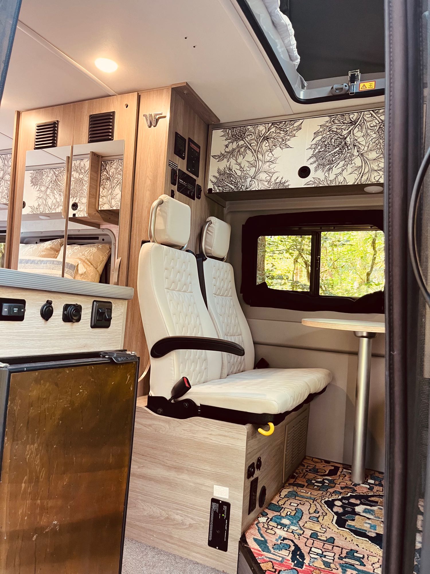 Inside a spacious RV rental: cozy seating, a dining table, ample storage with unique patterns, and a serene nature view. Ideal camper van.
