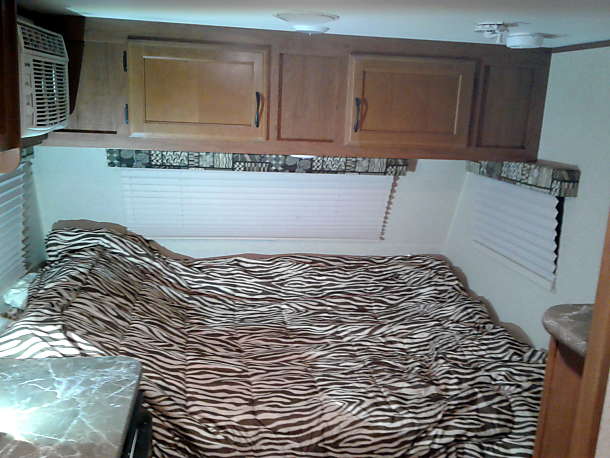 parked on grass beside a wooden fence with trees.|Rear of a white Jayco rv rental with spare tire