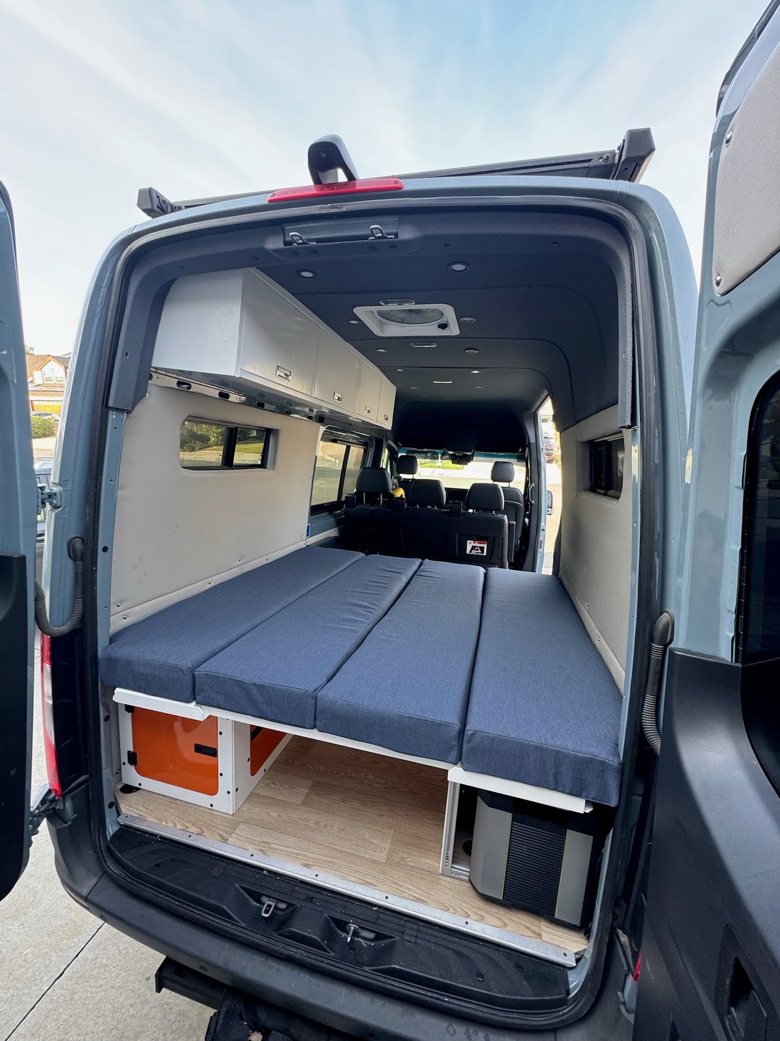 Spacious RV rental camper van interior with modular bed, overhead storage, and under-bed gear.