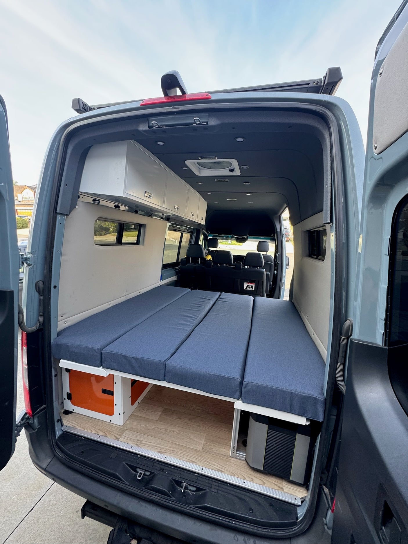 Spacious RV rental camper van interior with modular bed, overhead storage, and under-bed gear.