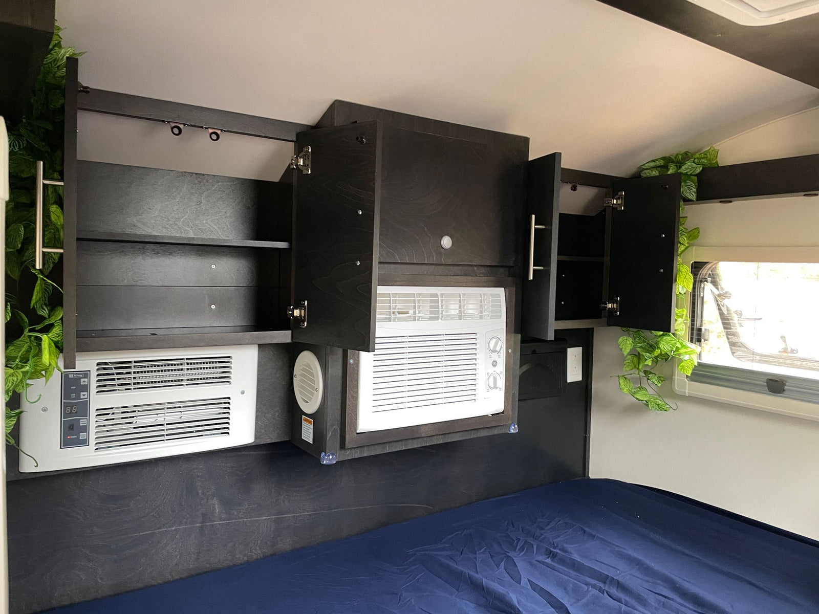 is parked under trees with a power cord connected.|This gray teardrop rv rental features an open outdoor kitchen with sink