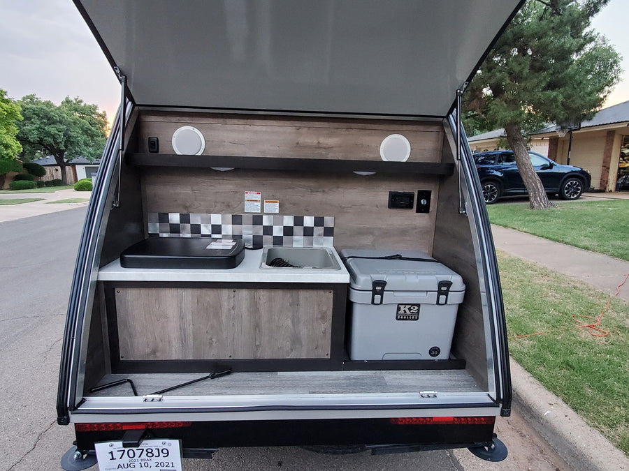 Open rear galley of an RV rental camper with outdoor kitchen: sink, stovetop, and K2 cooler, ready for camping trips.