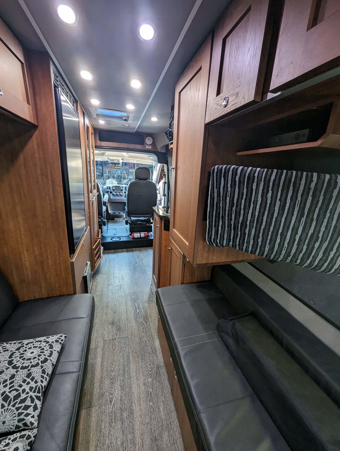 RV rental interior: A cozy camper van with wood cabinets, black seating, and modern lighting, looking towards the cockpit.