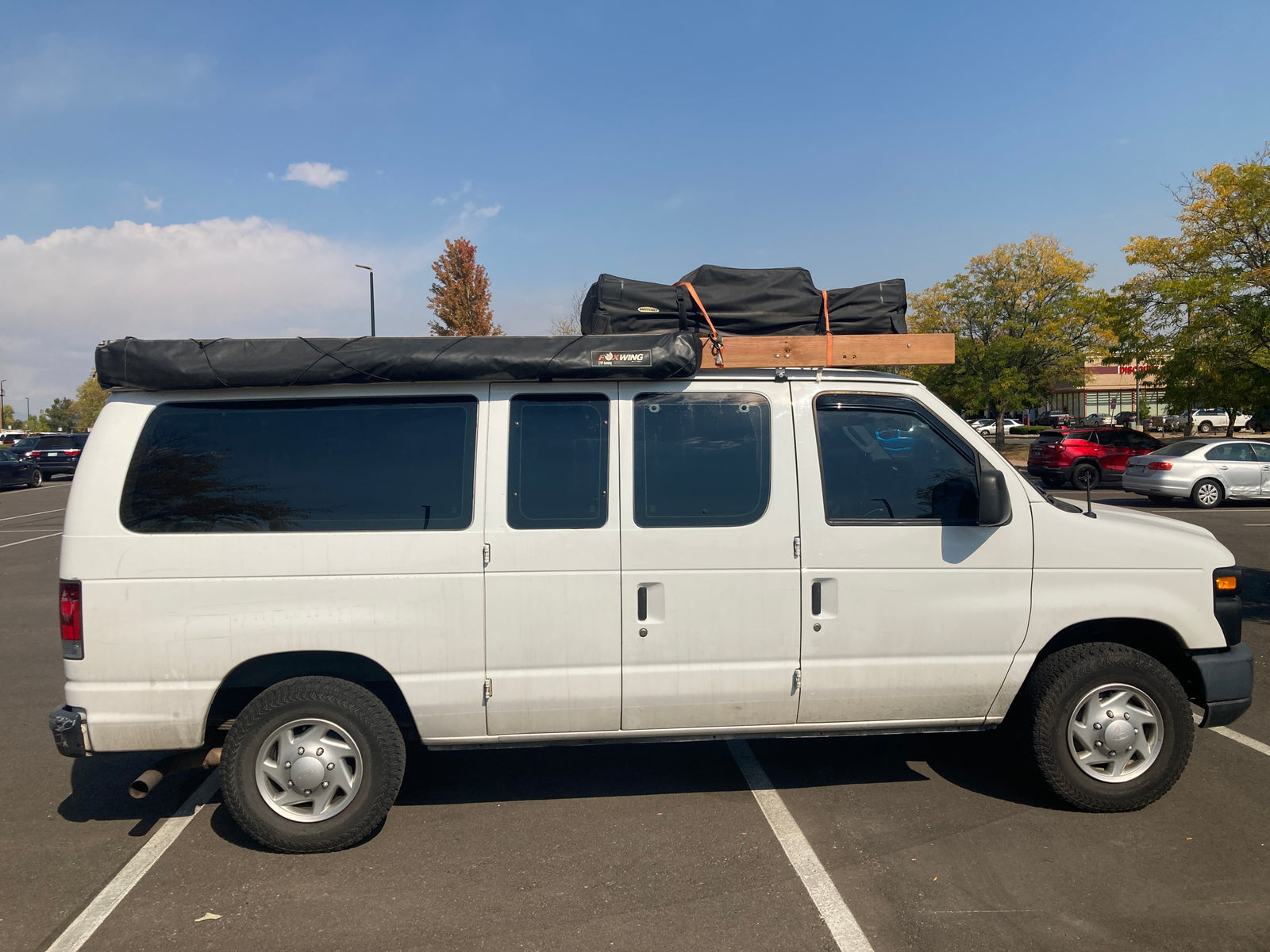 White camper van with roof rack and awning, parked on asphalt. An ideal RV rental for travel and adventures.