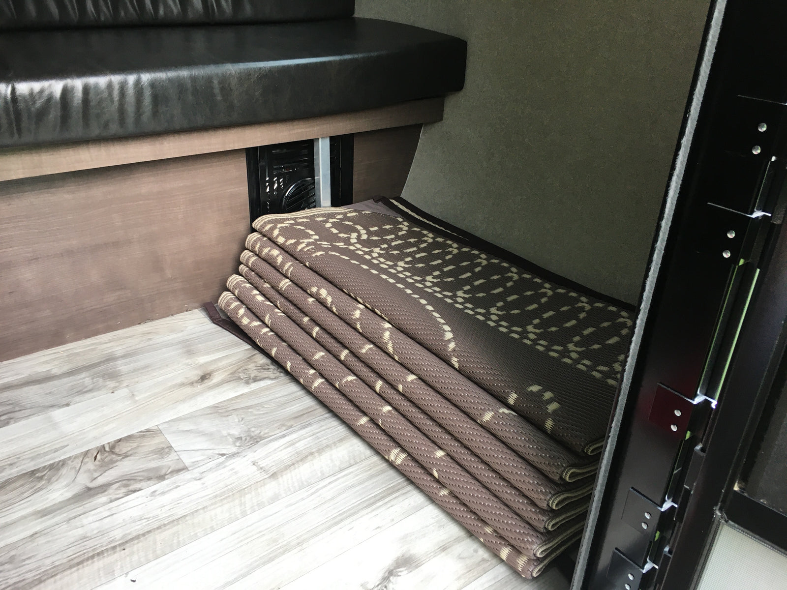 RV rental interior shows a dark bench, light wood floor, and neatly folded patterned mats beside a fan vent.