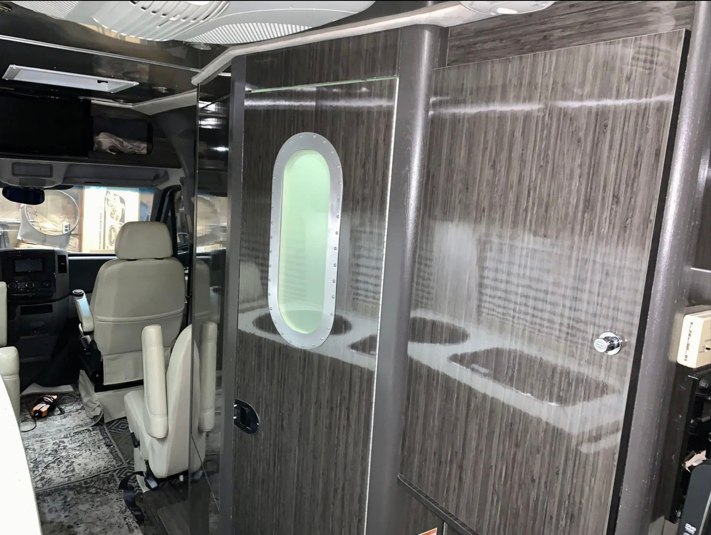 Interior of an RV rental, showcasing the driver's cabin with swivel chairs, and a modern wooden door with an oval porthole.