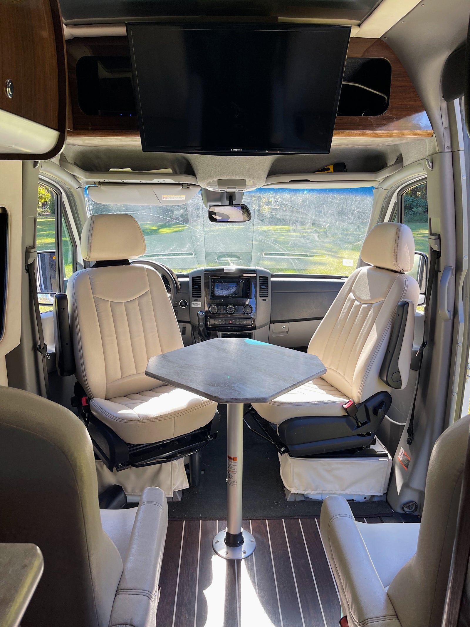 Spacious RV rental interior featuring swiveling front seats, a dining table, and an overhead TV for comfortable living.