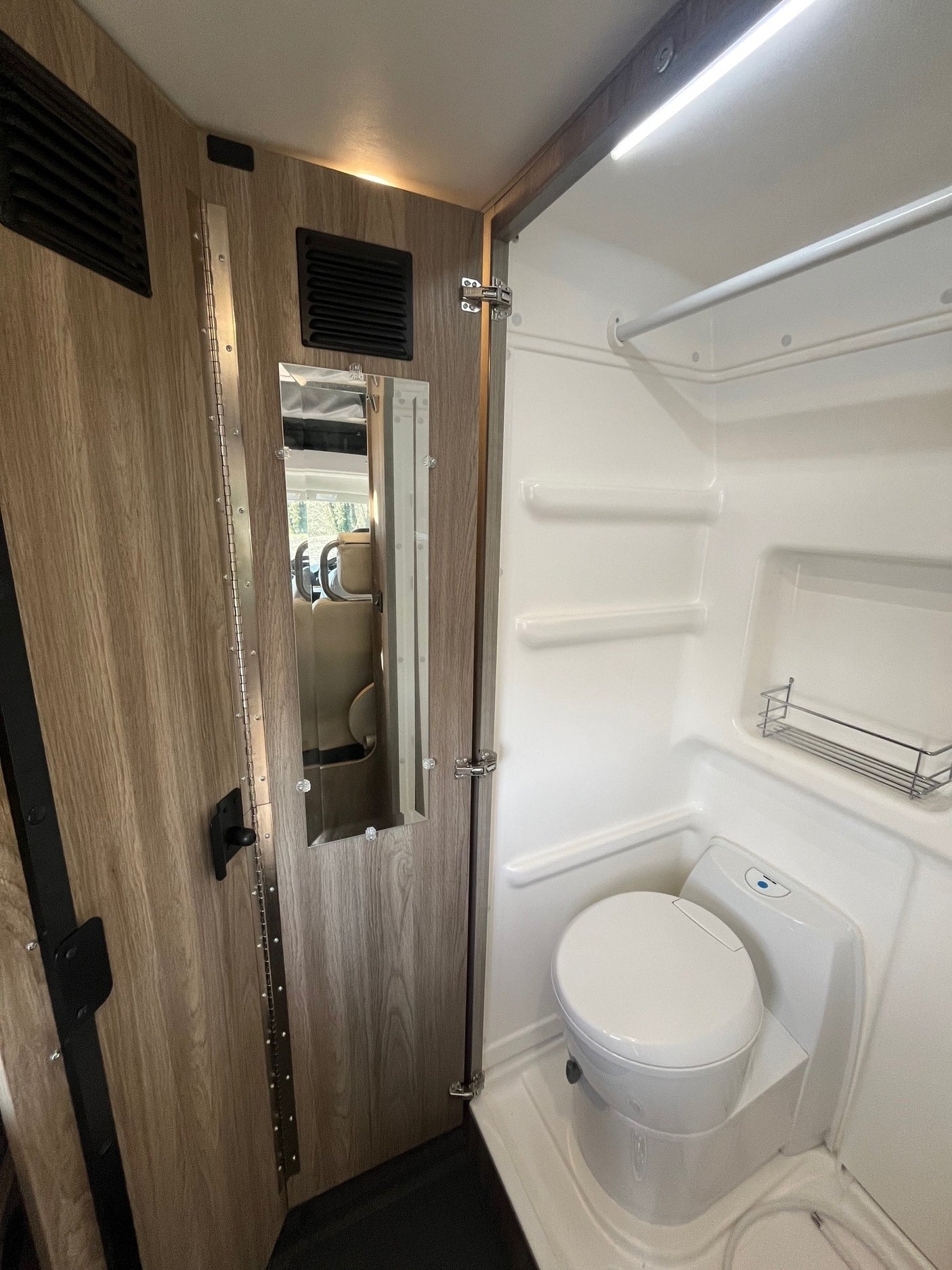 An RV rental's compact bathroom reveals a white toilet, shower space, and a door with an integrated mirror.