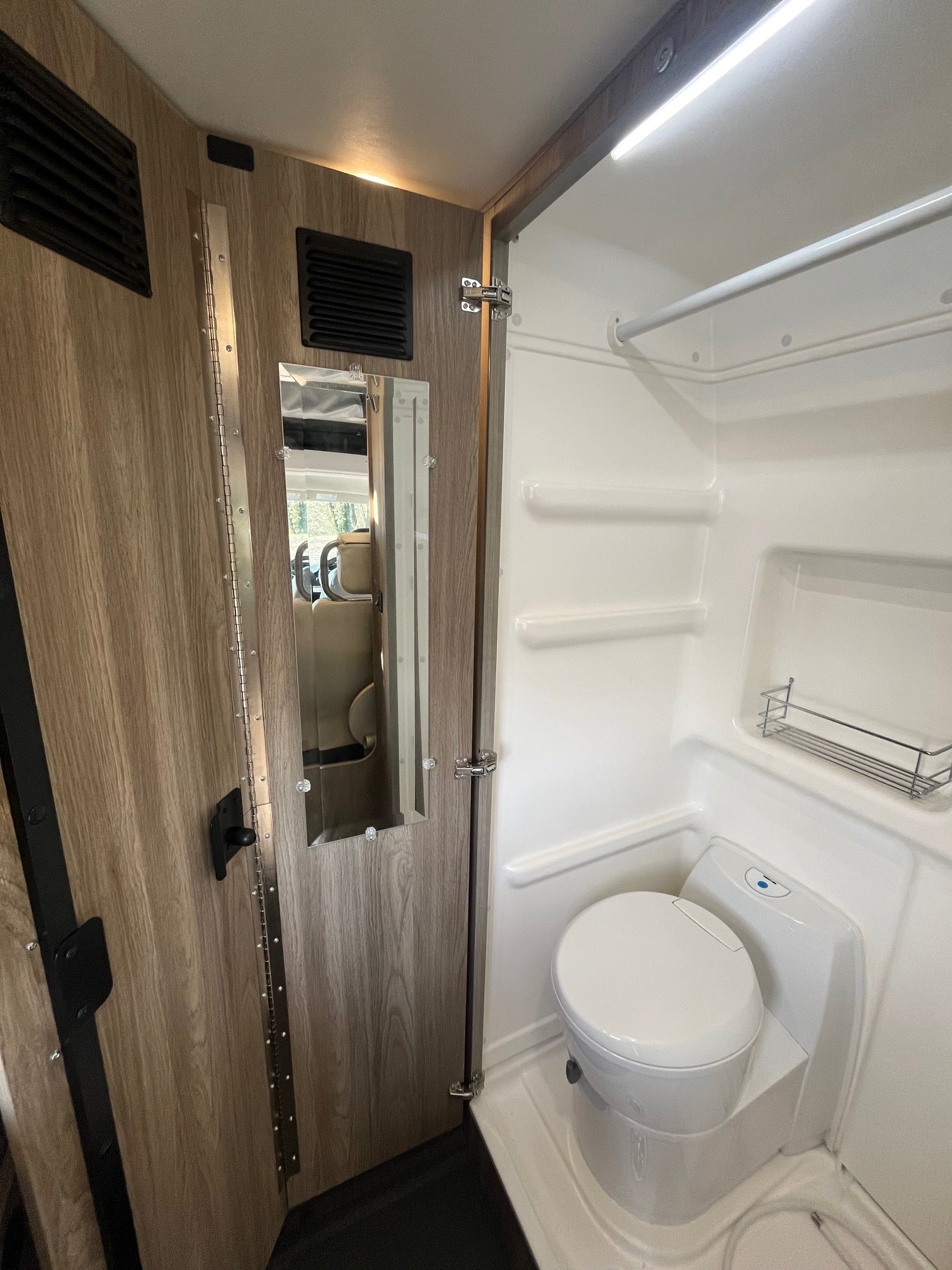 An RV rental's compact bathroom reveals a white toilet, shower space, and a door with an integrated mirror.