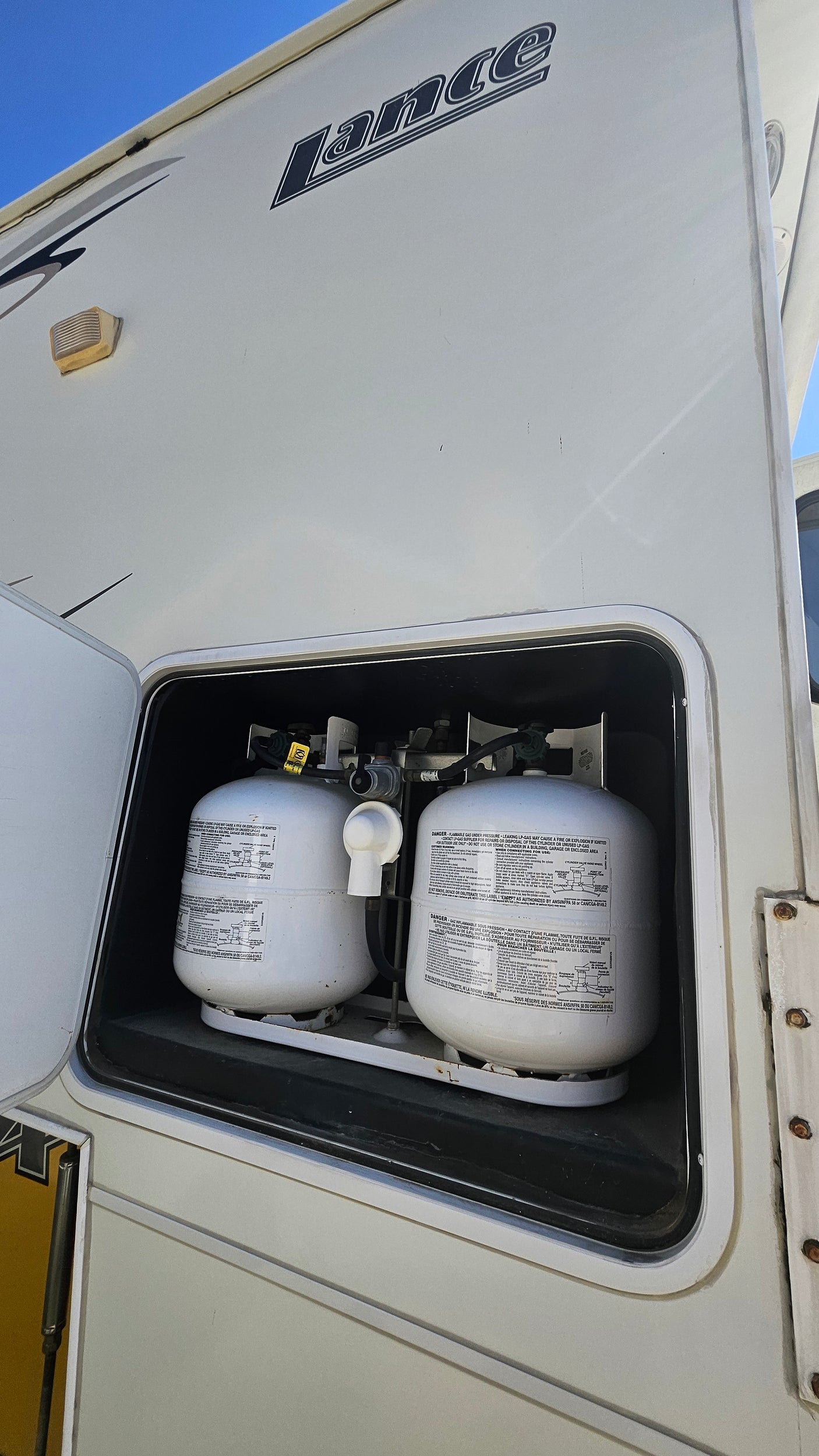 Inside an RV rental: two large white propane tanks secured in a side storage bay, essential for off-grid power and amenities.